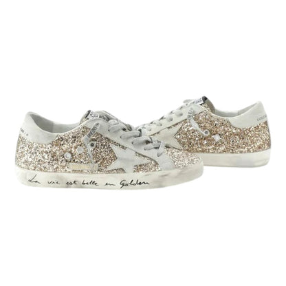 Luxurykicks.store Golden Goose Superstar low top sneakers in gold glitter with signature star and distressed sole.