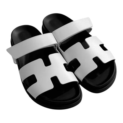 Luxurykicks.store Hermes Chypre sandals in white leather with a black footbed and iconic H-cutout strap design.