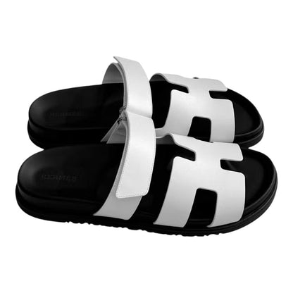 Luxurykicks.store Hermes Chypre sandals in white leather with adjustable straps and a black contoured footbed.