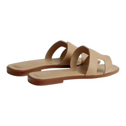 Luxurykicks.store Hermes Oran sandals in beige leather featuring the iconic H cut-out design on a flat sole.