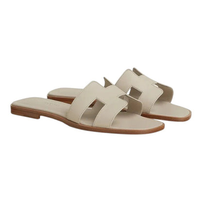 Luxurykicks.store Hermes Oran sandals in beige Nomade leather featuring the iconic H-cutout strap and flat sole.