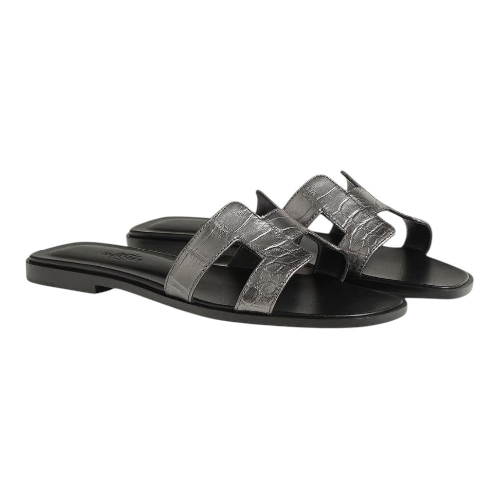 Luxurykicks.store Hermès Oran sandals in metallic grey with a crocodile-embossed leather finish and H-cutout strap.